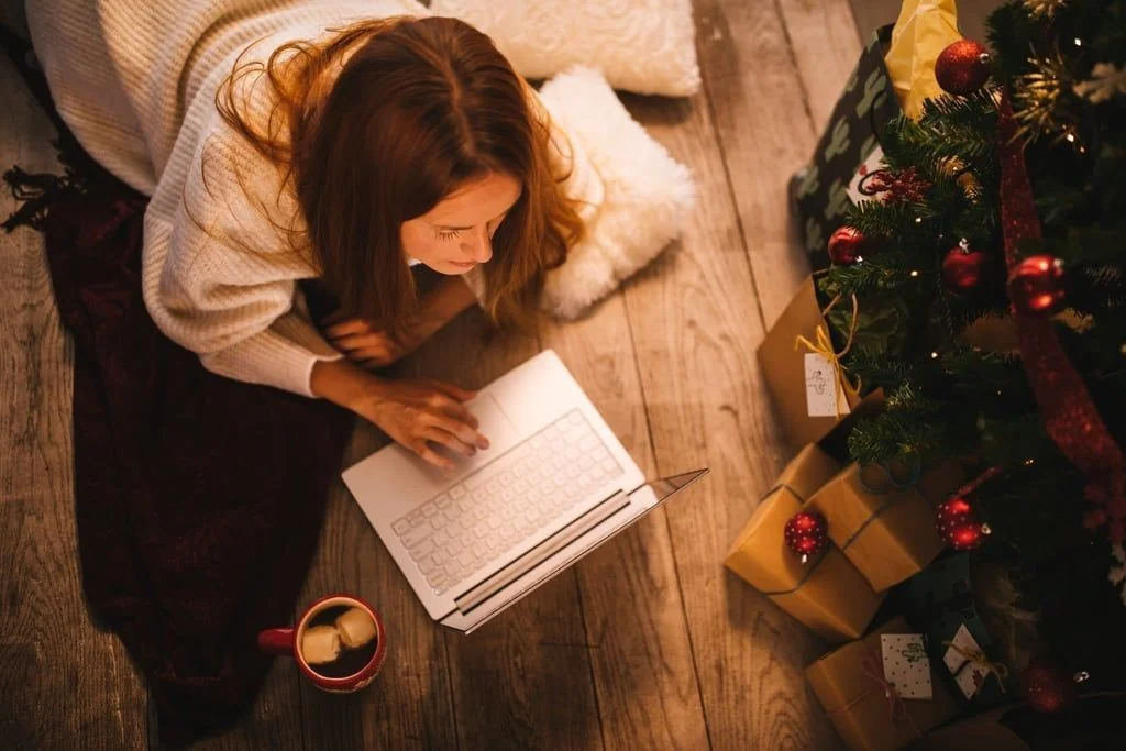 Frau mit Laptop neben Weihnachtsbaum